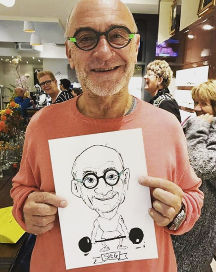 Een man met baard en bril toont blij een karikatuurtekening van zichzelf