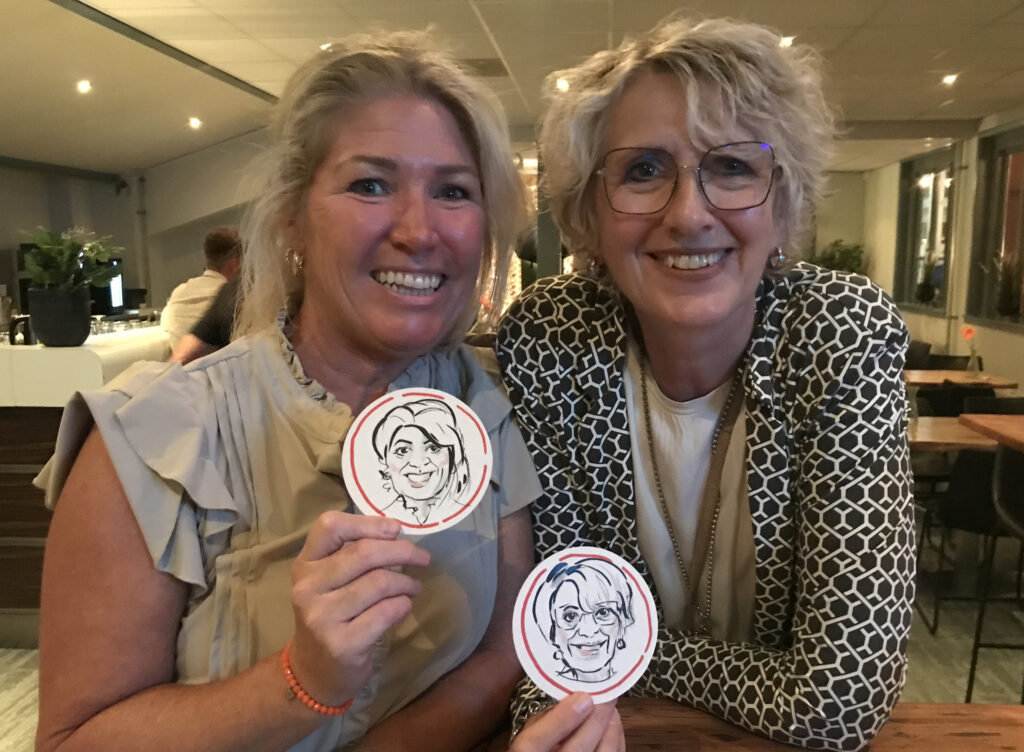 Twee dames op een feest houden bierviltjes in hun handen met hun karikatuur.